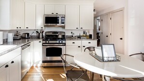 Een moderne keuken met witte kasten, roestvrijstalen apparatuur en een eethoek met een witte tafel en metalen stoelen.