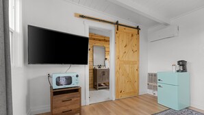 Ett rum med en platt-TV som är monterad på väggen, ett träskåp med lådor, ett ljusblått kylskåp och en skjutdörr i stil med en ladugårdsdörr.