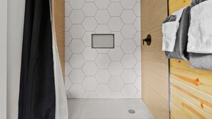 En dusch med ett hexagonalt kakelmönster, en trädörr och en handdukshängare med handdukar.
