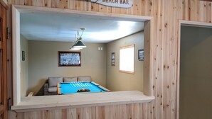 Et billardbord i et rum med træpaneler, et skilt der siger "Beach Bar", og billeder i rammer på væggen.