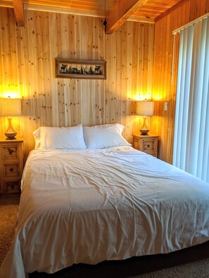 Une chambre à coucher aux murs lambrissés, avec un grand lit, deux tables de chevet dotées de lampes et un tableau encadré accroché au mur.