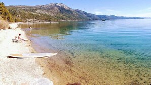 A clear lake with a sandy beach, a surfboard, and mountains in the background.