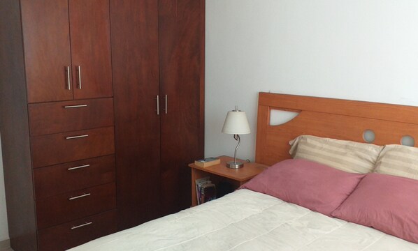 A bedroom with a bed, a nightstand, a lamp, and a wooden wardrobe.