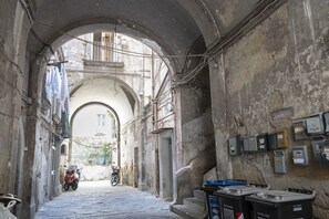 An arched corridor with a motorcycle parked at the end, electrical boxes on the walls, and a sign indicating non-recyclable waste. - Maiorani Family Apartment by Wonderful Italy (Napoli)