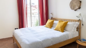 A neatly made bed with white and yellow pillows, a wooden headboard, and a small bedside table with a book. - Maiorani Family Apartment by Wonderful Italy (Napoli)
