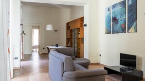 A living room with a grey sofa, a TV on a stand, and a bookshelf. - Maiorani Family Apartment by Wonderful Italy (Napoli)