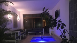 Ein Poolbereich mit blau beleuchtetem Pool, einer Sitzecke und einem an der Wand befestigten Fernseher.
