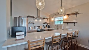A modern kitchen with a large island, wooden chairs, pendant lights, and built-in appliances. - Lake Tillery- Beautiful sunrises, large screened porch, and newly renovated home (Norwood)