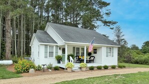 A single-story house with a porch, a flag, and potted plants. - "Bee Haven" Cottage Retreat Near Colonial Williamsburg (Gloucester)