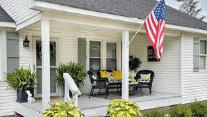 A porch with two potted plants, a chair, and a table. - "Bee Haven" Cottage Retreat Near Colonial Williamsburg (Gloucester)