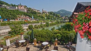 Una terraza con mesas al aire libre con vistas a un río y una colina con edificios.