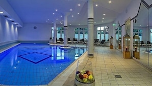Una amplia piscina interior con baldosas azules brillantes, sillones de descanso y faroles decorativos.