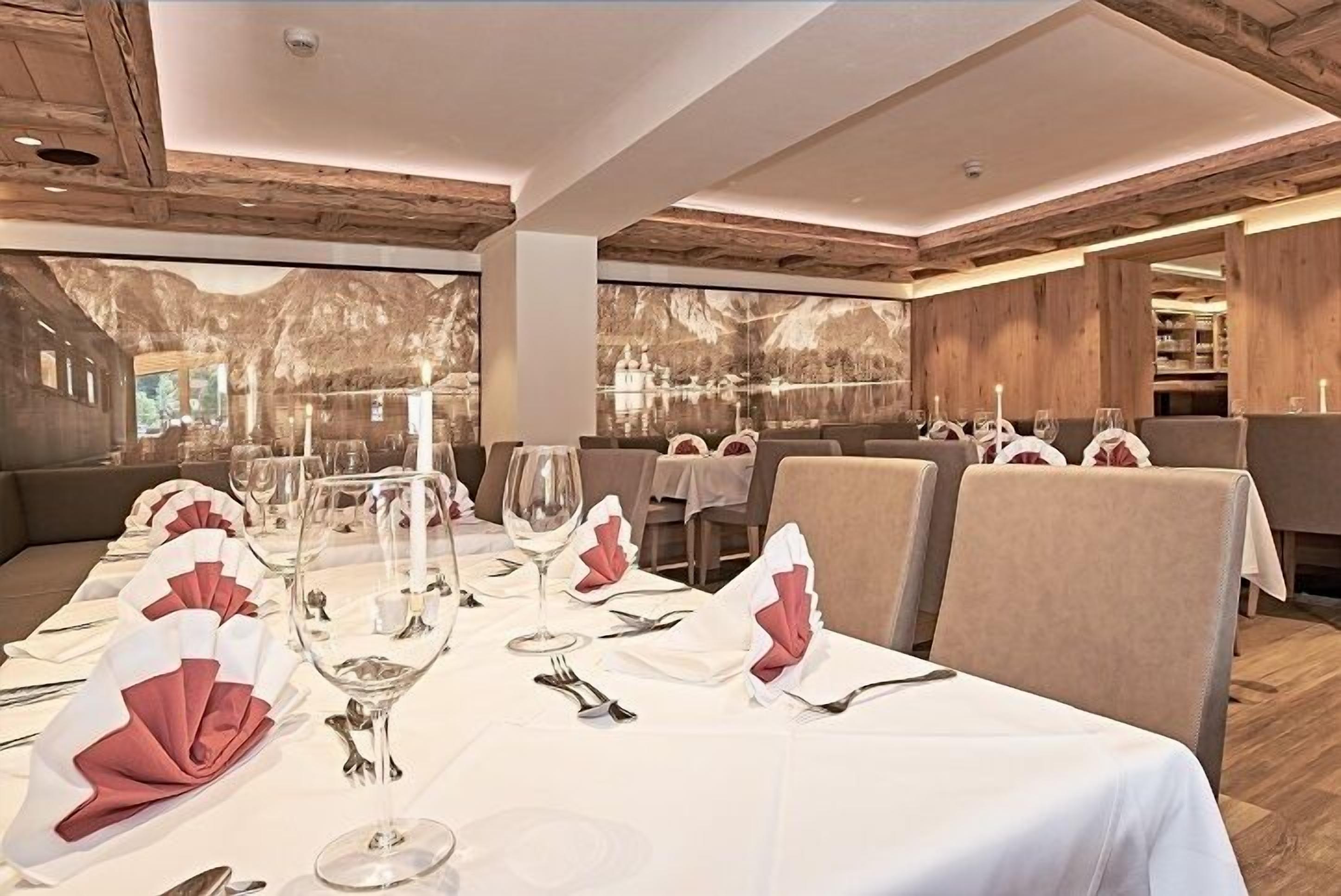 A restaurant with a long table set for dining, wooden ceiling beams, and a large window with a mountain view.