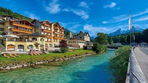 Un hôtel situé au bord de la rivière, doté de balcons, offrant une vue dégagée sur une montagne et arborant un mât de drapeau.