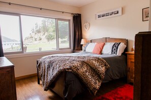 Ein Schlafzimmer mit großem Fenster, einem Bett mit Leopardenmuster-Decke und einem Holzkopfende.