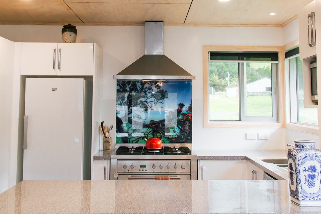 Une cuisine moderne avec des meubles blancs, une hotte en acier inoxydable et une grande fenêtre offrant une vue sur l’extérieur.