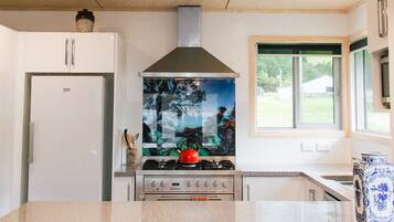 Une cuisine moderne avec des meubles blancs, une hotte en acier inoxydable et une grande fenêtre offrant une vue sur l’extérieur.