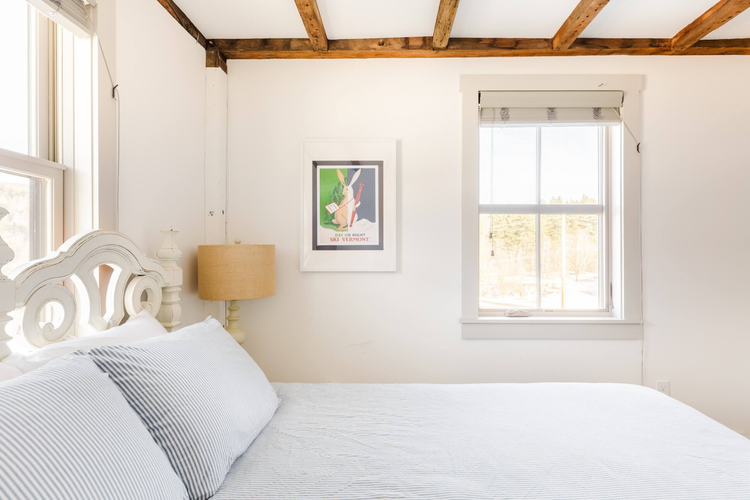 Ein Schlafzimmer mit einem Bett, einem Fenster, einem gerahmten Bild und einer Lampe.