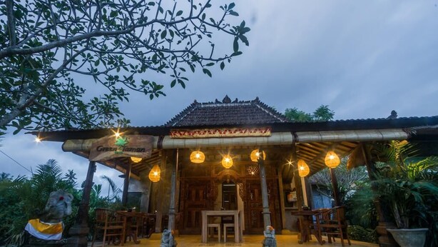Une construction traditionnelle en bois, avec un toit recouvert de tuiles, une véranda abritée ornée de lanternes suspendues, et une petite table avec des chaises devant.
