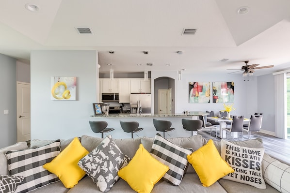 A modern living room with a sofa, a dining area, and a kitchen in the background.