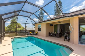 A swimming pool with a covered patio area, outdoor seating, and a view of the surrounding trees.