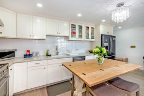 A modern kitchen with white cabinets, a wooden dining table, and a chandelier.