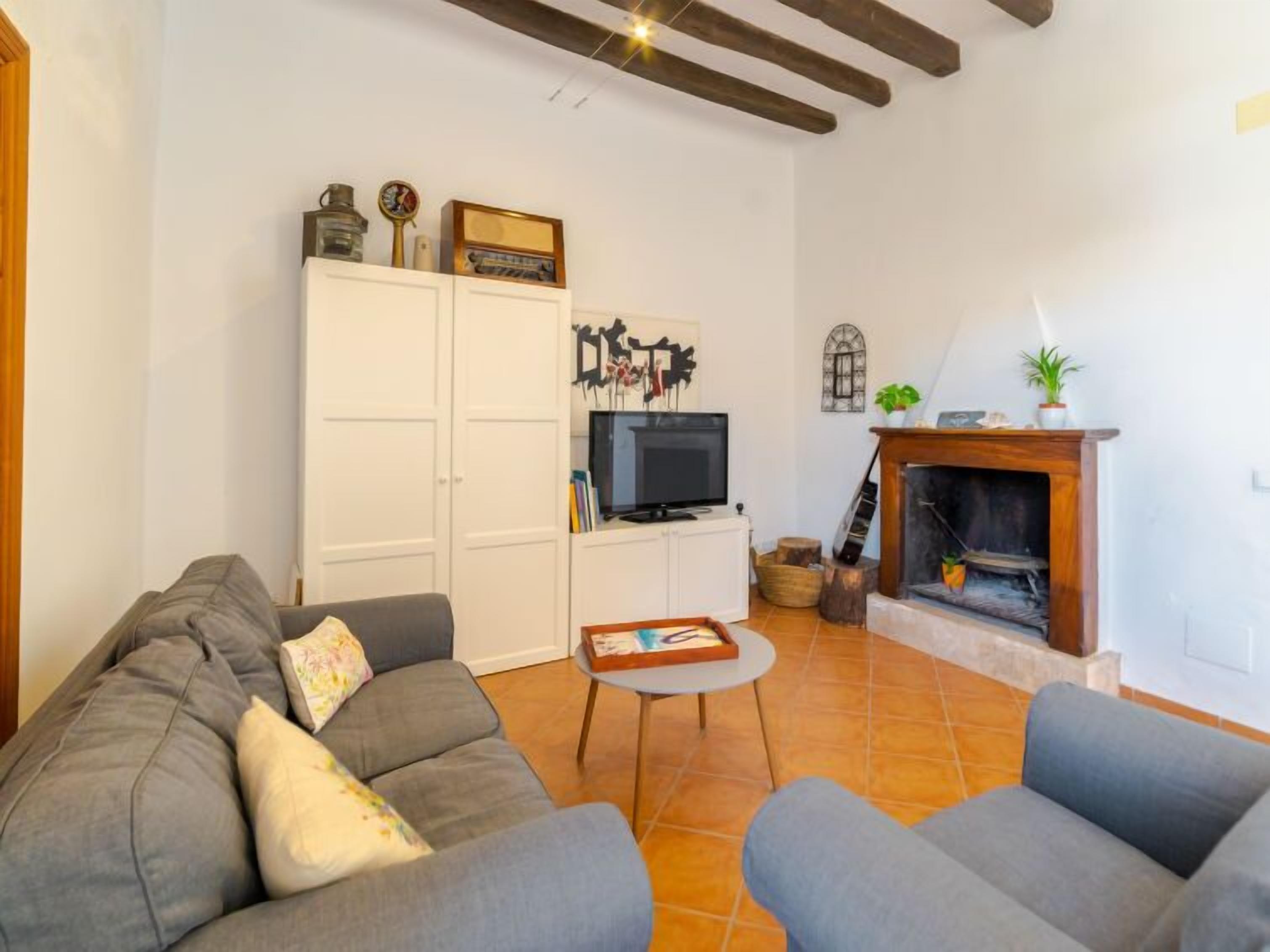 A living room with a grey sofa, a television, a fireplace, and a white cabinet with decorative items.