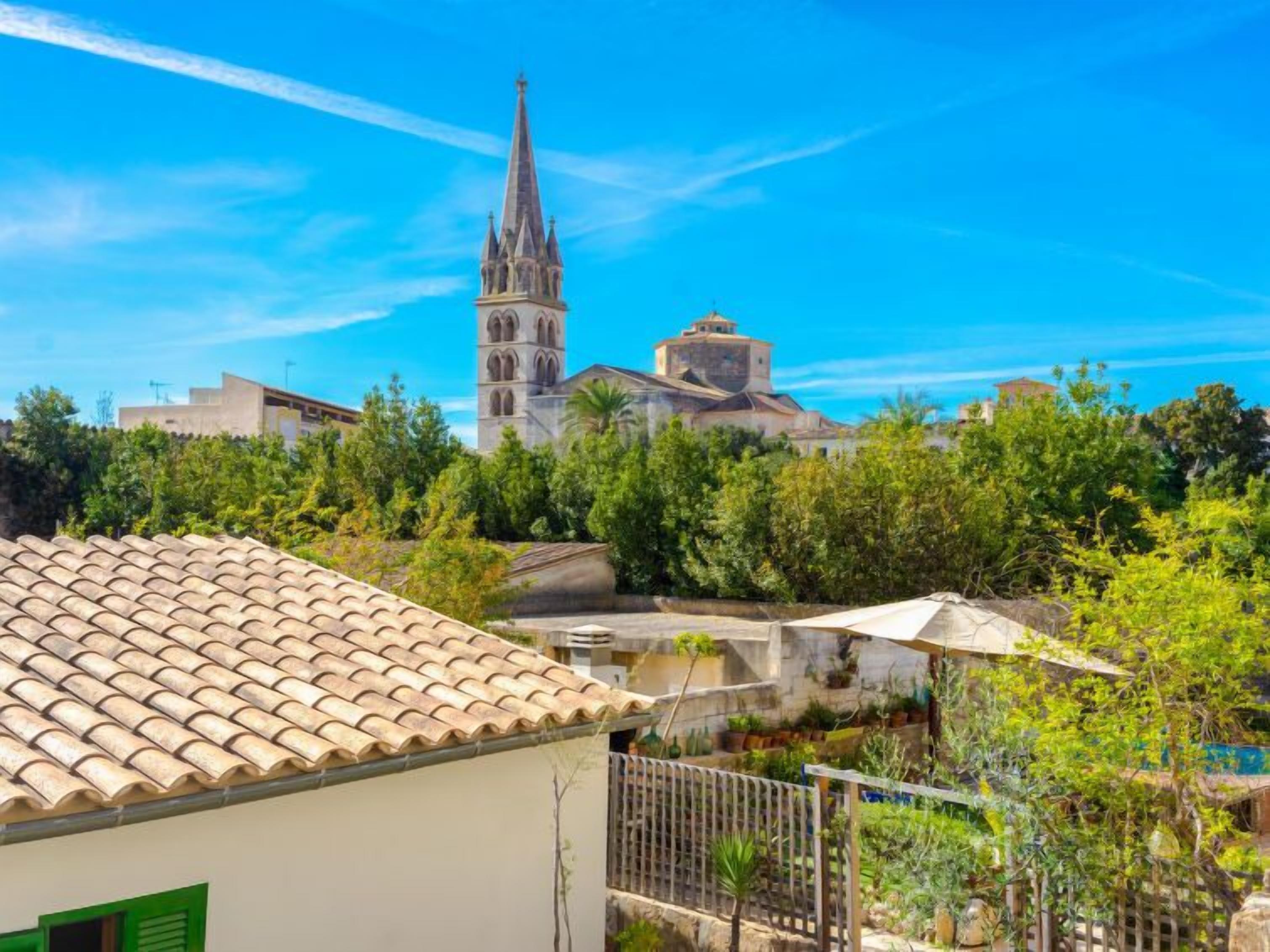 On peut voir une église avec un clocher élevé et un bâtiment plus petit surmonté d’un dôme, le tout entouré de verdure et de bâtiments résidentiels.