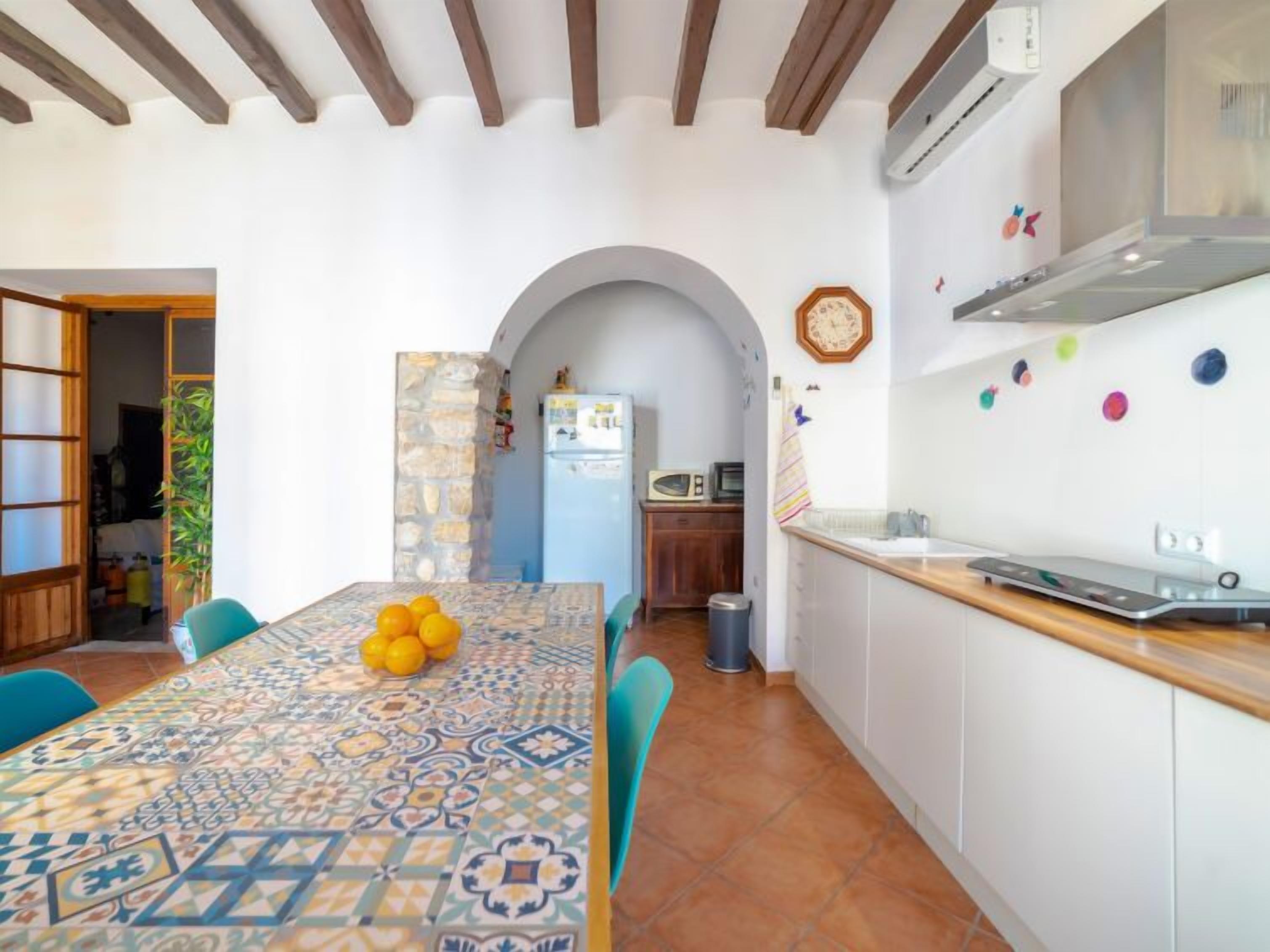 A kitchen with a tiled backsplash, a wooden ceiling, and a dining area with a patterned tablecloth and chairs.
