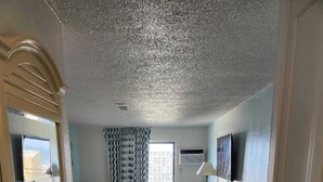 A hotel room with a bed, a desk, a chair, a mirror, and a bathroom with a sink and toilet. - Sea Mist 51301 (Myrtle Beach)