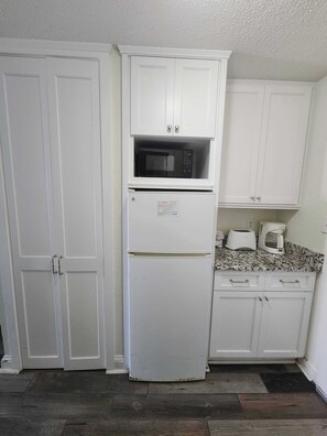 A kitchen with white cabinets, a microwave, a refrigerator, and a coffee maker.