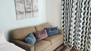 A room with a sofa, pillows, a bed, a wooden floor, and a curtain with a leaf pattern. - Sea Mist 51301 (Myrtle Beach)