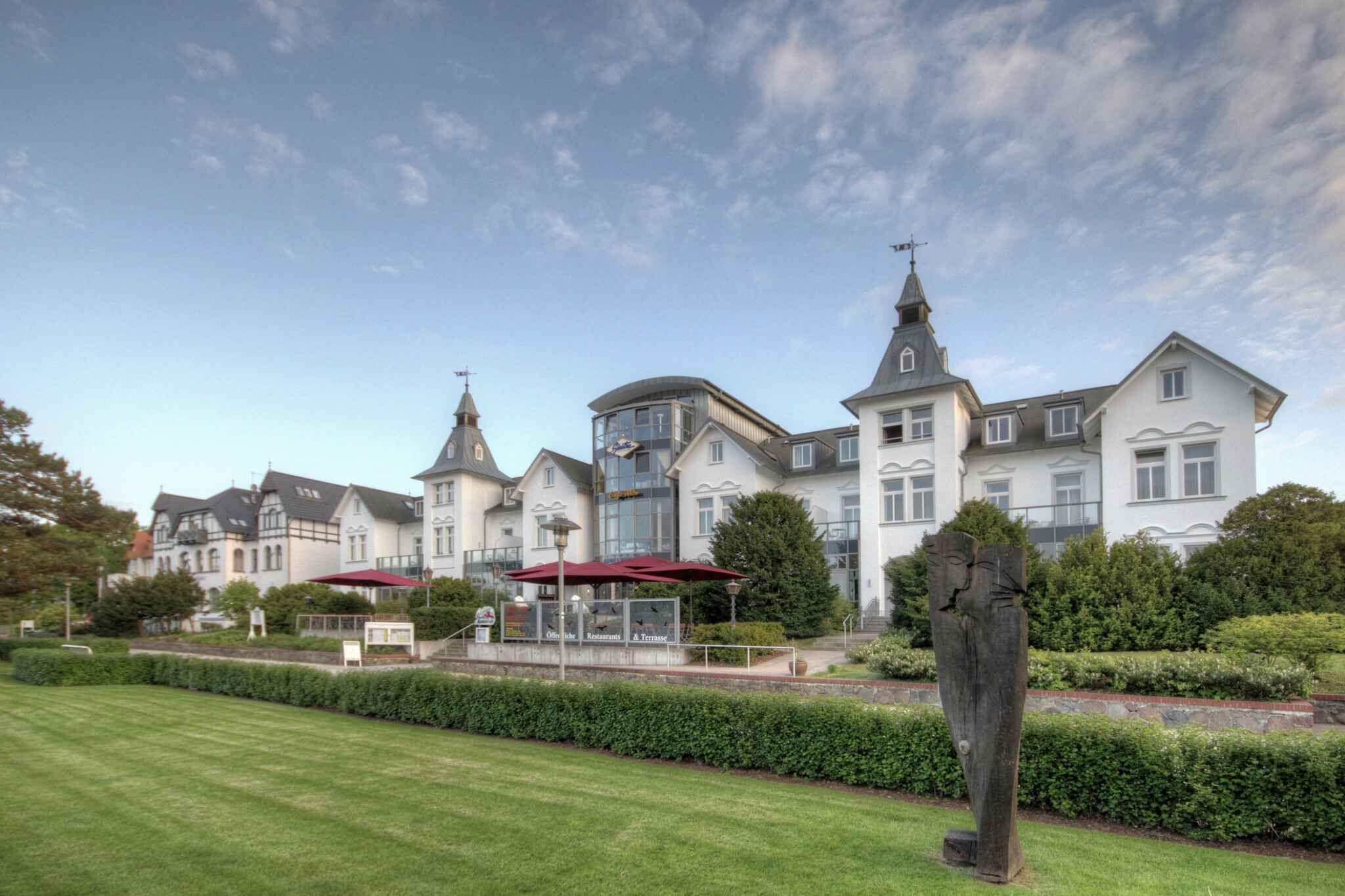 A large, historic building with multiple towers and a well-maintained garden in front.