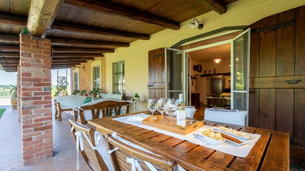 A covered outdoor dining area with a brick column, wooden benches, and a table set for a meal. - Stunning private villa for 8 people with private pool, WIFI, A/C, TV and terrace (Asti)