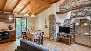 Una sala de estar acogedora con chimenea de piedra, vigas de madera, comedor con mesa preparada para cuatro personas y cocina con electrodomésticos modernos.