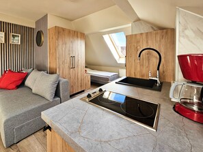 A compact living space with a kitchenette, a sofa, a dining table, and a window providing natural light.