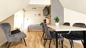 Un dormitori tipus loft modern amb sostre inclinat, un llit integrat, zona de menjador amb taula i cadires, i un televisor penjat a la paret.