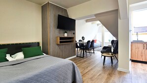 Un dormitori modern amb un llit gran, televisió penjada a una paret amb ratlles, i zona de dinar amb cadires i taula.