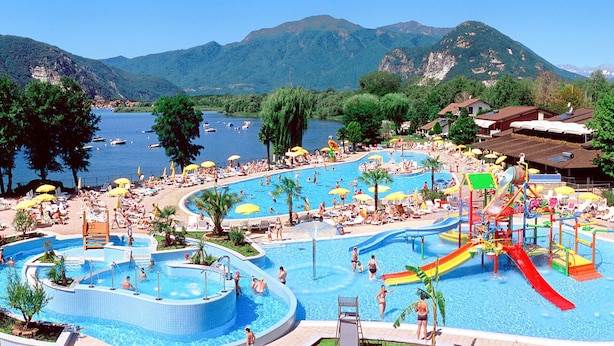 A large outdoor swimming pool with multiple lanes and a water slide, surrounded by trees and mountains. - Lovely apartment for 6 guests with pool, WIFI, TV and balcony (Verbania)