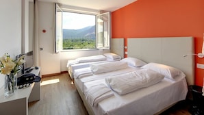 A hotel room with two beds, a desk with a phone and a vase of flowers, and a window with a mountain view. - Lovely apartment for 6 guests with pool, WIFI, TV and balcony (Verbania)