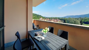 A balcony with a table, chairs, and a view of a town and hills. - Lovely apartment for 6 guests with pool, WIFI, TV and balcony (Verbania)