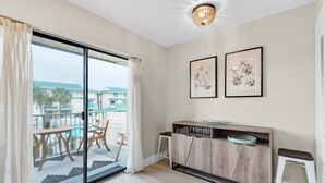 Una camera moderna con una porta scorrevole in vetro che dà su un balcone, un mobile in legno con bicchieri e due quadri floreali appesi alla parete.