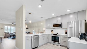 Una cucina moderna con elettrodomestici in acciaio inossidabile, mobili bianchi e illuminazione a sospensione.