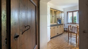 A wooden door with a heart-shaped handle, leading into a kitchen with wooden cabinets, a window, and a dining area with chairs and a table. - Beautiful apartment in villa for 6 guests with TV and patio (San Daniele Del Friuli)