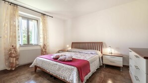Een slaapkamer met een bed, nachtkastje, kast, raam met gordijnen en een radiator.