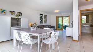 Een moderne keuken met witte kasten, een eettafel met witte stoelen en uitzicht naar buiten.