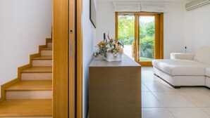 Una sala de estar moderna con una escalera de madera, un sofá blanco y un ventanal que da a un jardín.