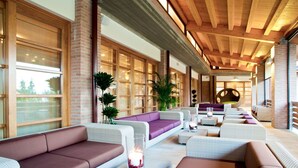 Amplia zona de estar interior con varios sofás y sillones, ventanas grandes y techo de madera.