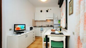 A compact kitchen with white cabinets, a microwave, a small dining table with chairs, and a television displaying a cartoon.