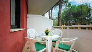 A balcony with a white table and four white chairs, each with a green cushion.